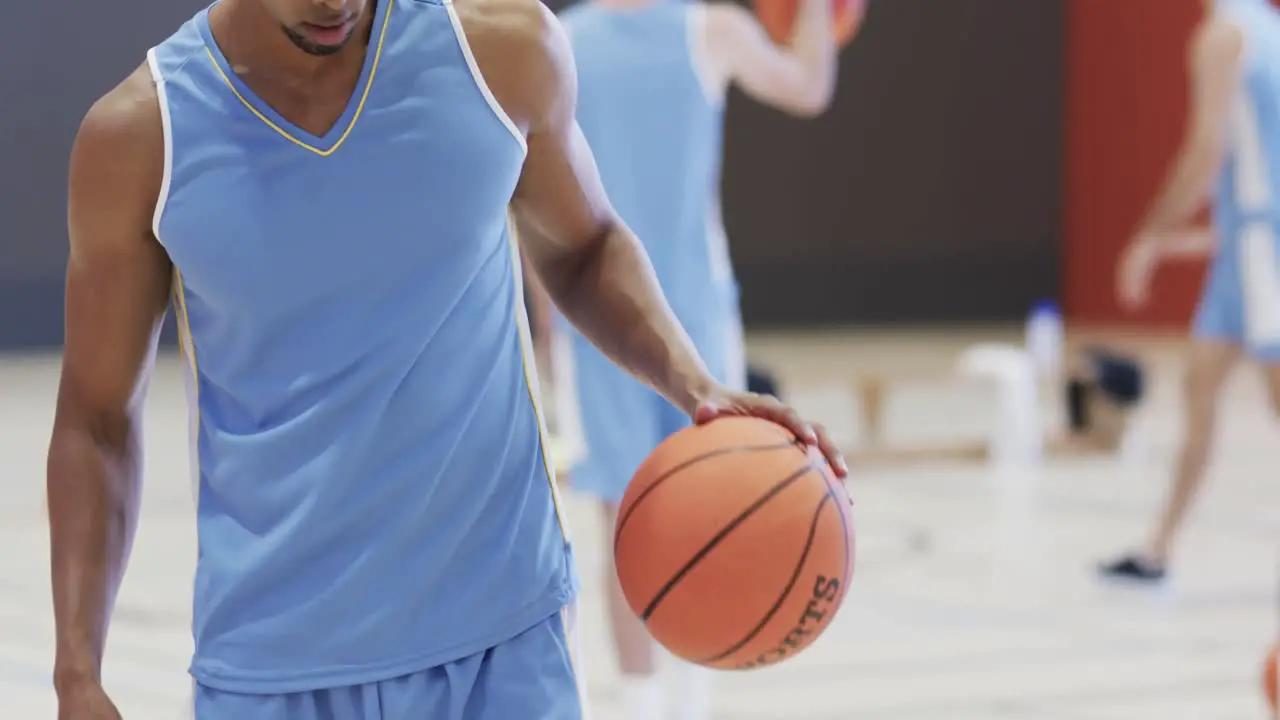 Biracial male basketball player with ball during team training on indoor court in slow motion