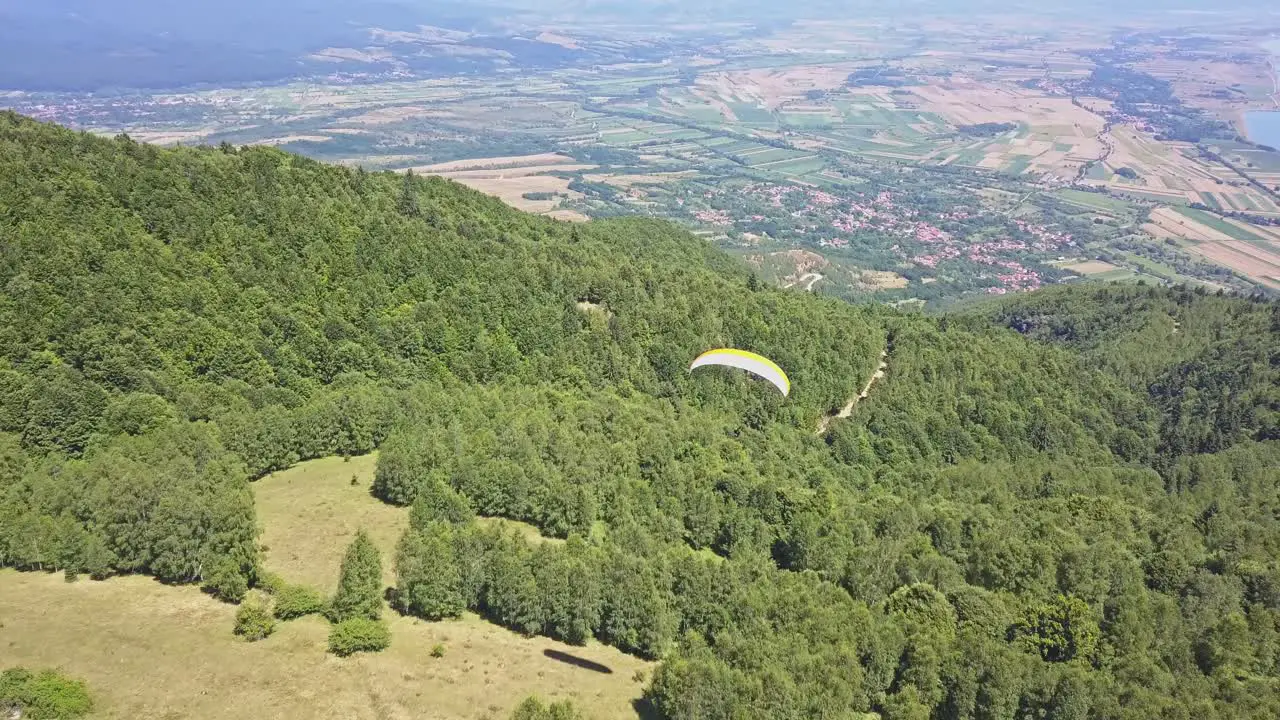 Scenic view following paraglider over green trees with valley and town at base of mountain