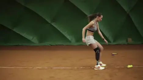 Athlete on the leg prosthesis runs around the court setting tennis balls in the corners Trainings Sportswear Indoors