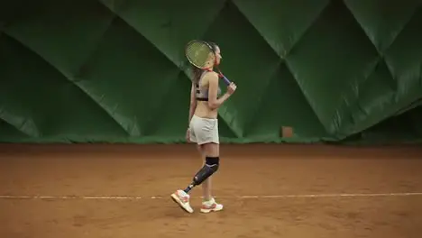 Disabled young woman is walking through the tennis court with racket Stands in the stance Ready for match