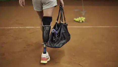 Smiling girl athlete comes to tennis training pulls out a racket and goes to the court Leg prosthesis Slow motion