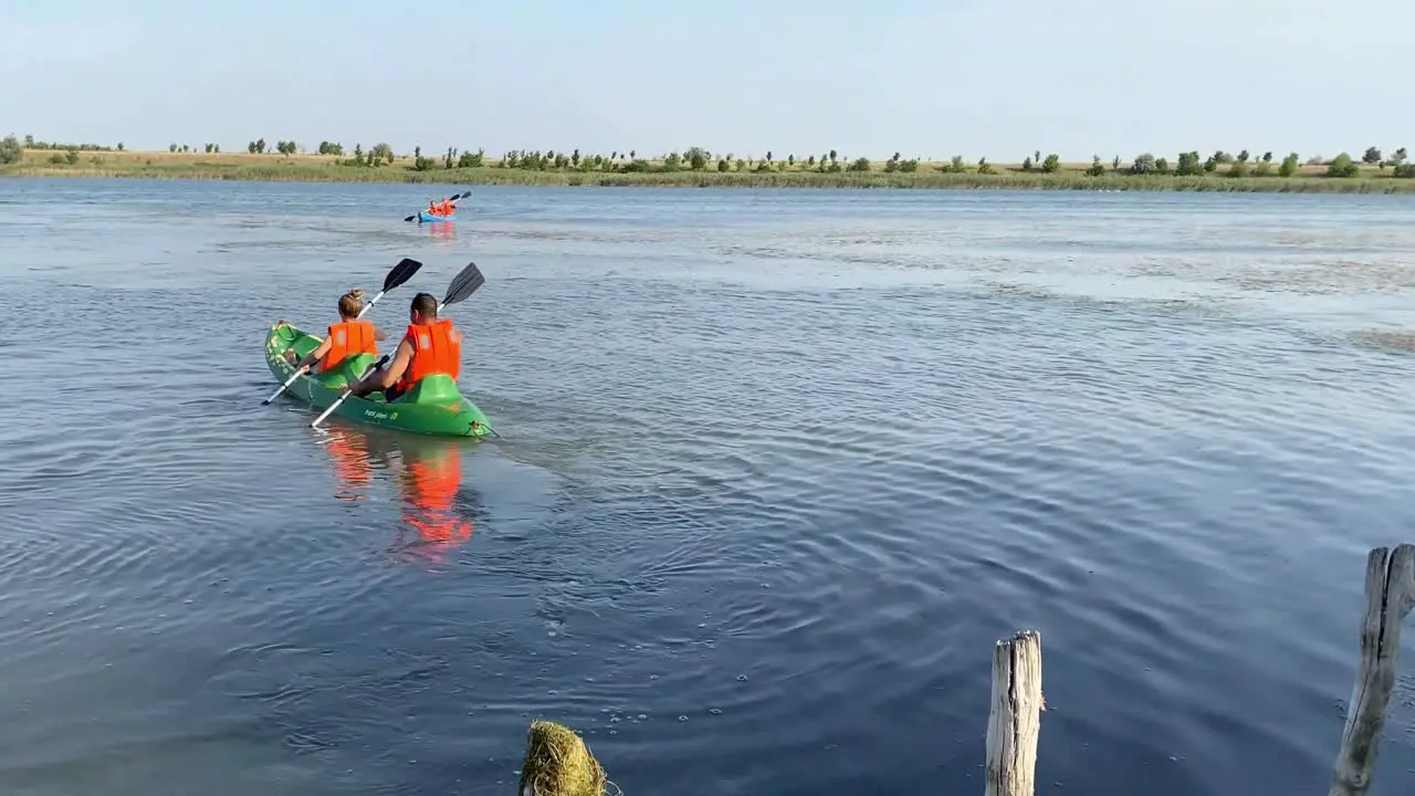 Back view of pair in orange lifejackets kayaking on lake in wildlife