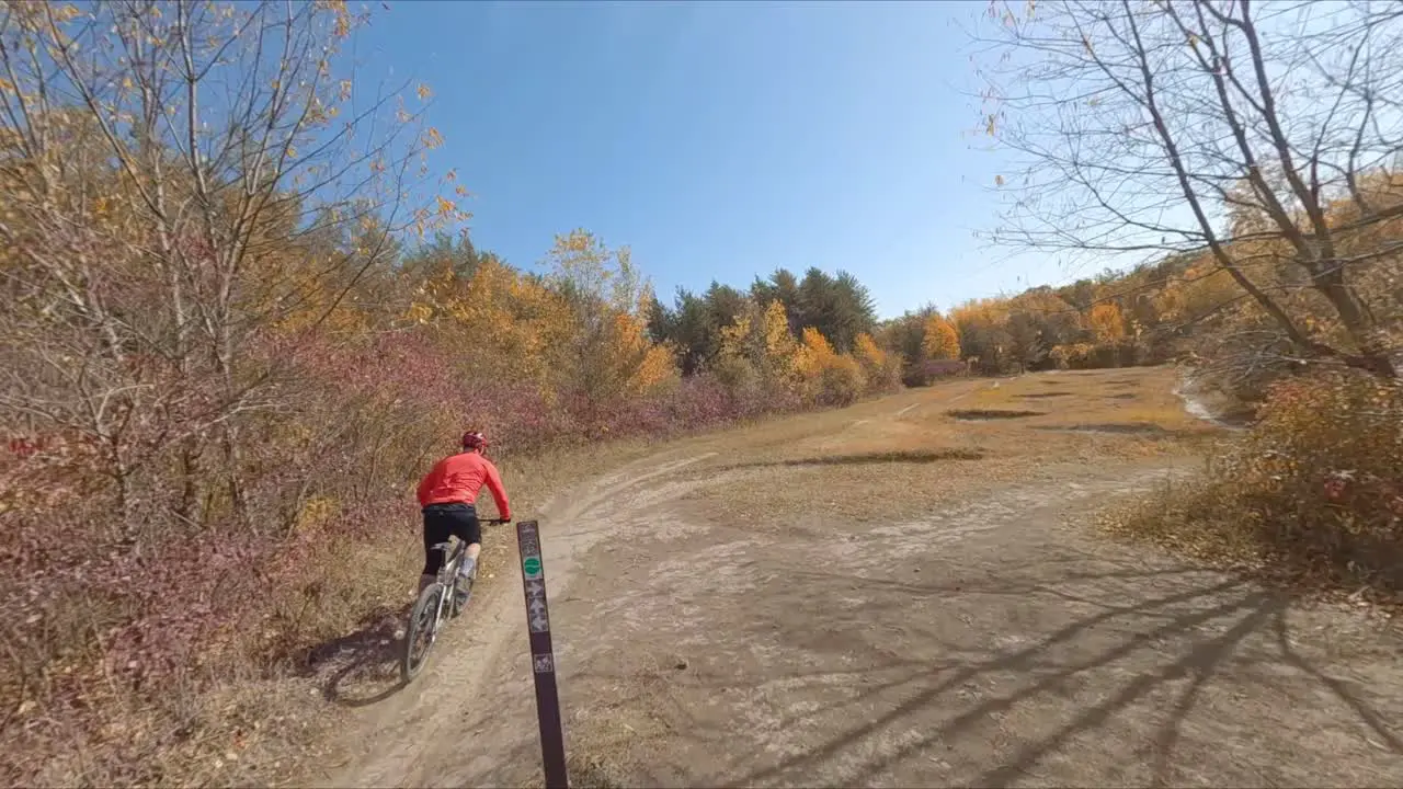 FPV drone following male mountain biker biking on dirt trail during autumn day