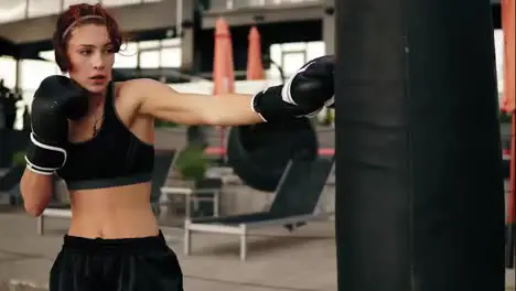 Attractive athletic female boxer in gloves punching a boxing bag Workout outside Female boxer training in boxing gloves Shot in 4k