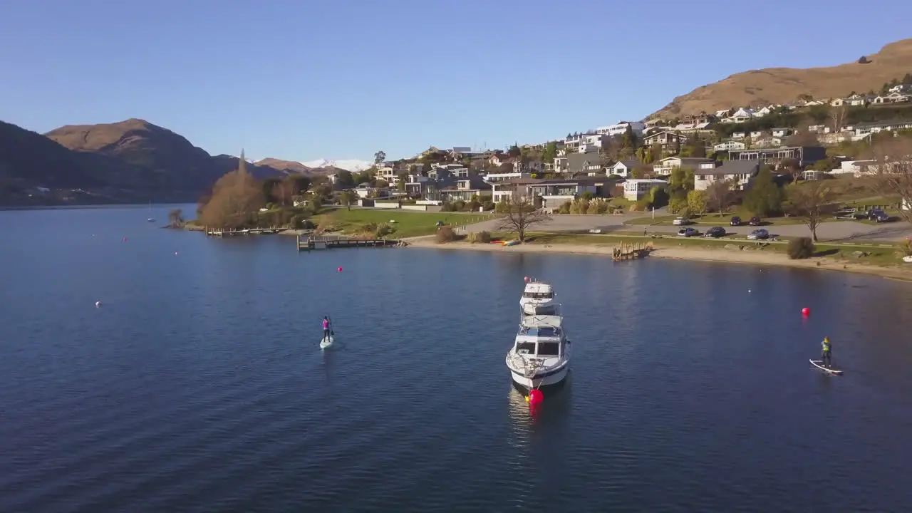 Paddleboarder in paddling in a blue bay next to moored boats