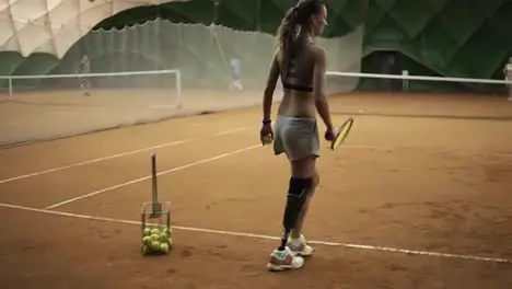 Two beautiful girls practicing The handicapped girl in short shorts takes the ball from the basket and makes the first serve of the ball Indoor tennis court Back view