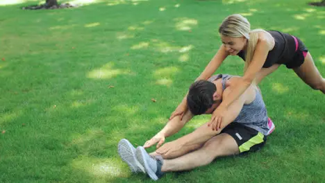 Woman sport trainer help fitness man stretching legs in summer park