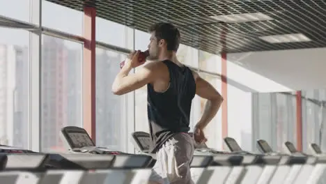 Runner man drinking water from bottle at intensive training on treadmill machine