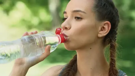 Fitness woman drinking water from bottle after running exercise in city park