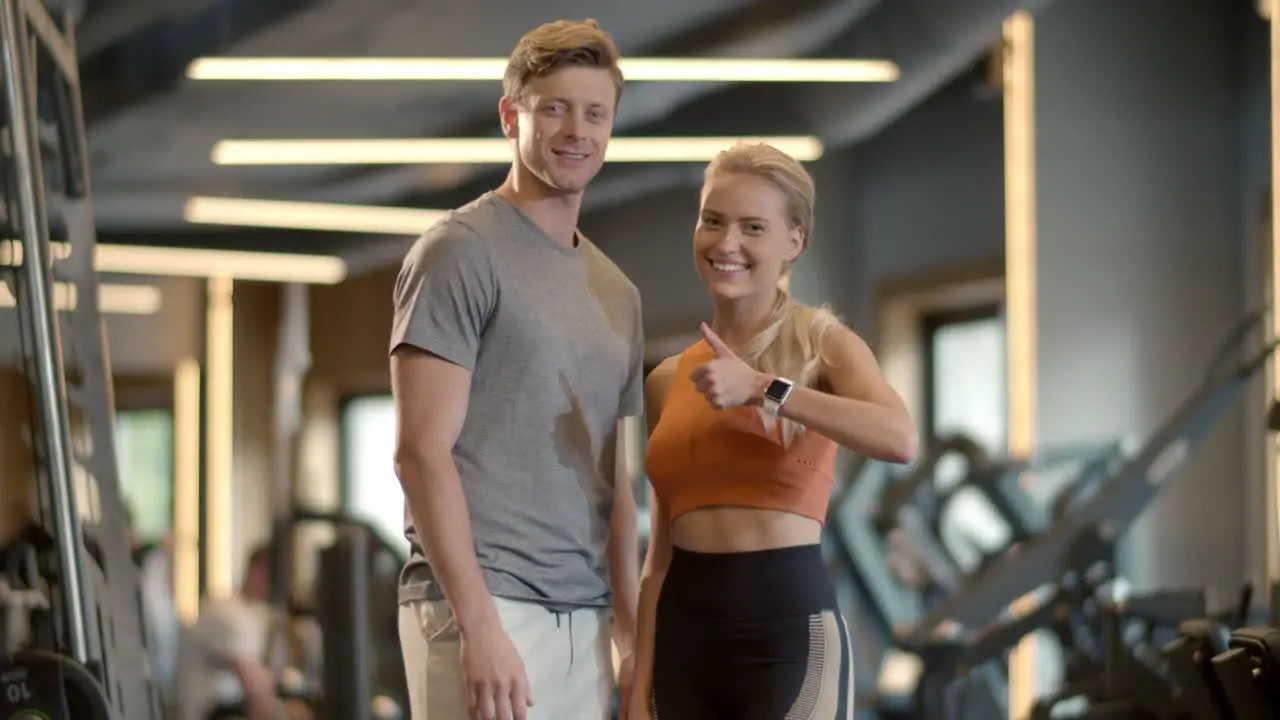 Excited couple enjoying results in sport club Fit girl showing like sign at gym