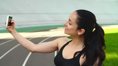 Sport woman taking selfie photo on mobile phone at stadium track