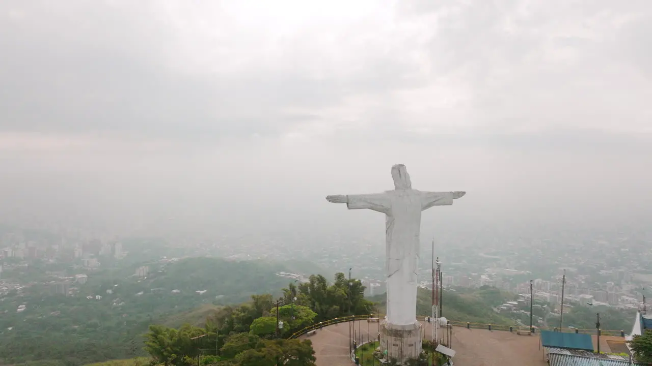 Slow aerial flyover footage of the Cristo Rey statue that flies right past the head of the statue in the city of Cali Colombia