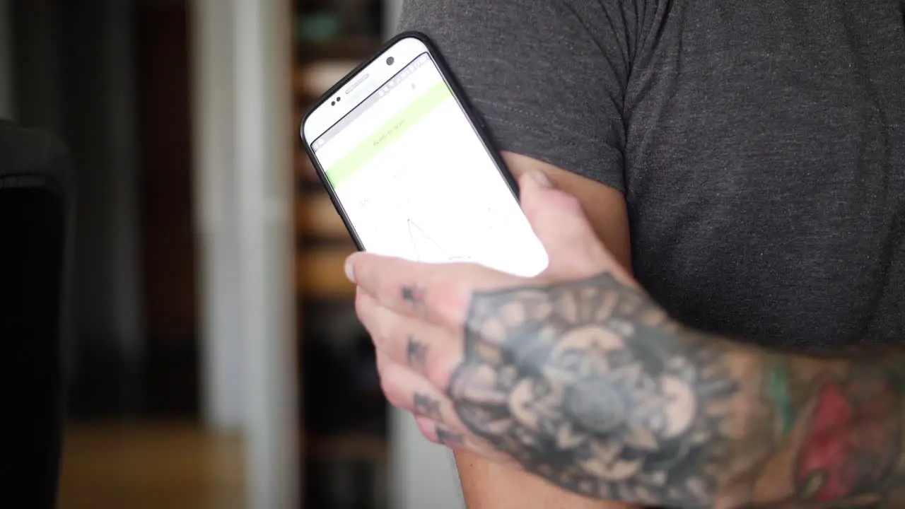 A young man with diabetes checks his blood glucose levels in his home with his smartphone and glucose reading sensor on his arm