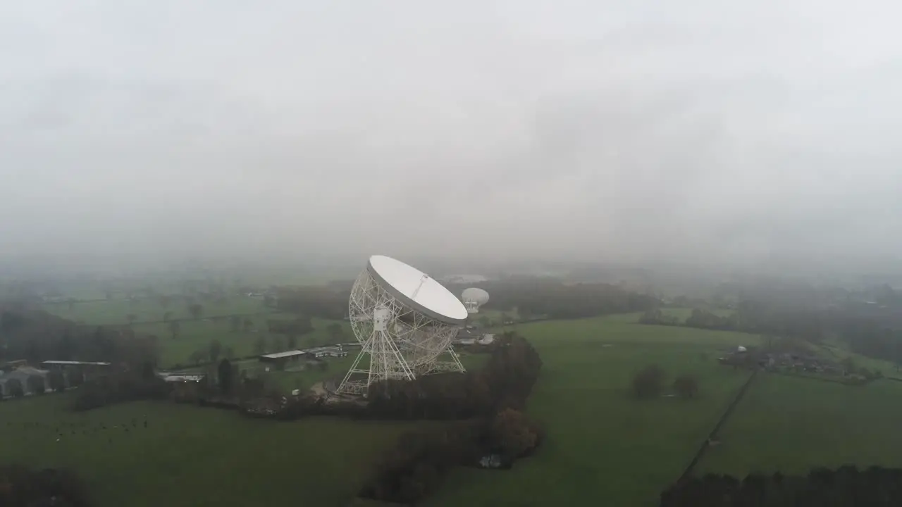 Aerial Jodrell bank observatory Lovell telescope misty rural countryside pull away tilt up