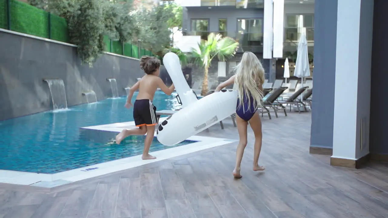 girl and boy run by the pool with pool toy in their hands