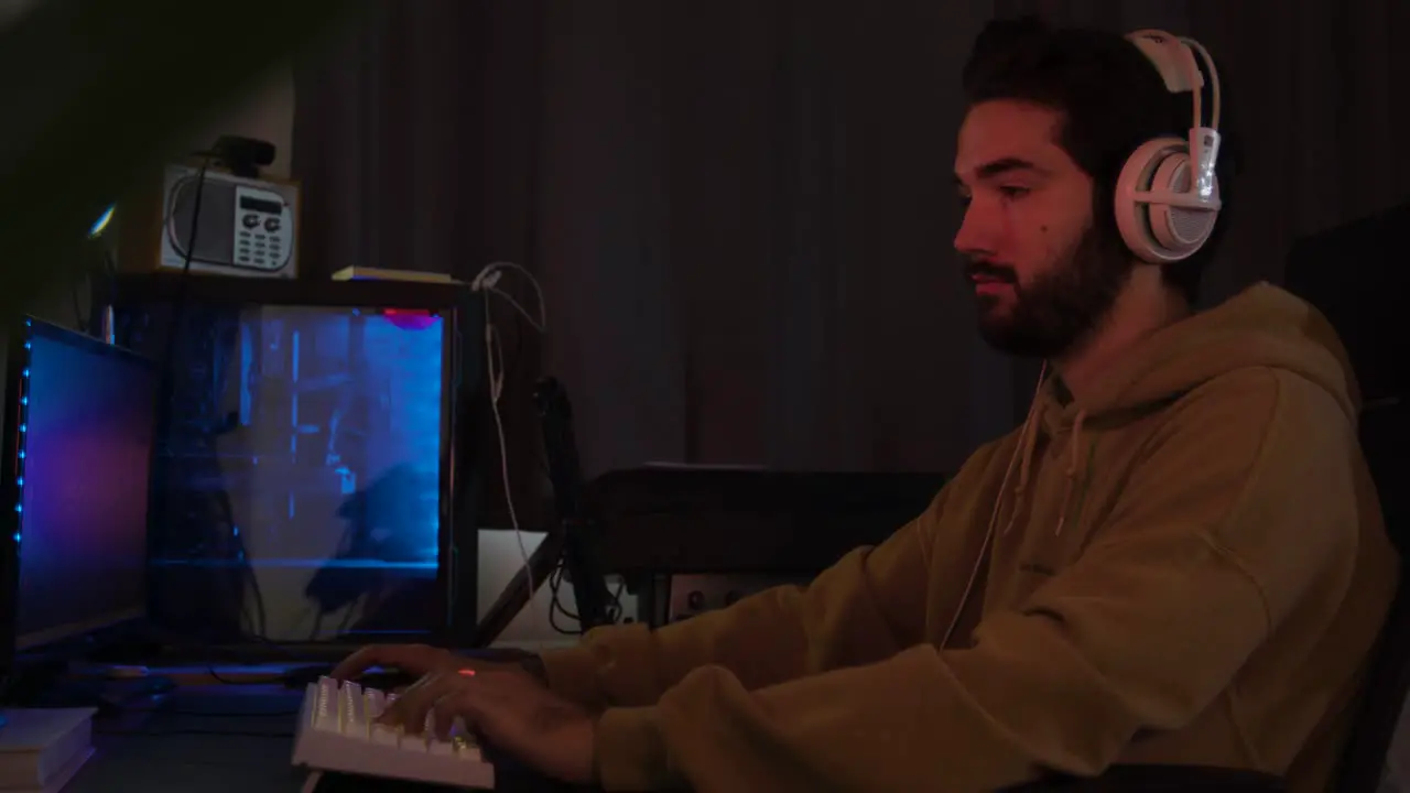 Male using PC gaming and concentrating while wearing white headphones in a darkened room