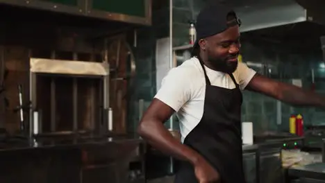 A Black person dances at work in a doner market against the backdrop of a barbecue Man in black apron and white t-shirt having fun at work