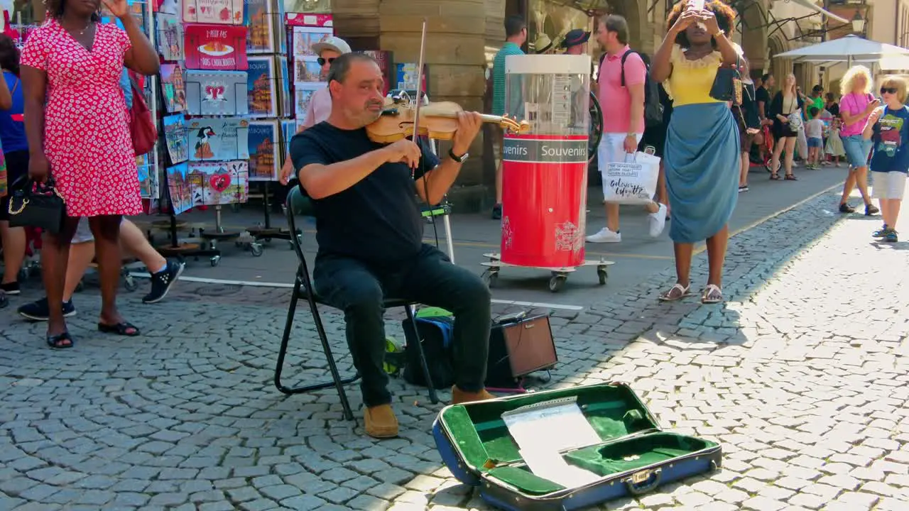 older man sitting on chair playing violin on the city market square in Strasbourg