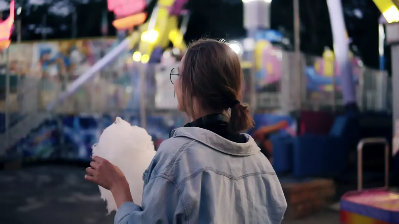 Traking Footage Of A Young Blonde Girl Walking In The Amusment Park Eating White Candy Cotton