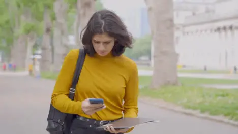 Tracking Shot of Young Student Walking Whilst Looking at Her Smartphone