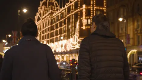 People Walking Towards Exterior Of Harrods Department Store In London Decorated With Christmas Lights