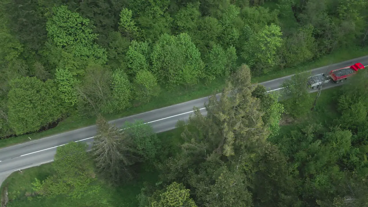 A truck and tow loaded with gravel driving through the forest on an asphalt road