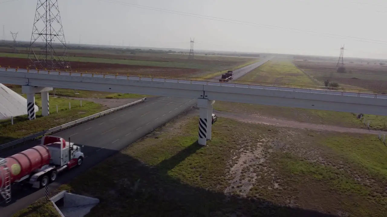 Trailers on asphalt road in Reynosa Tamaulipas Mexico with a bridge on a sunny day drone shot 4k