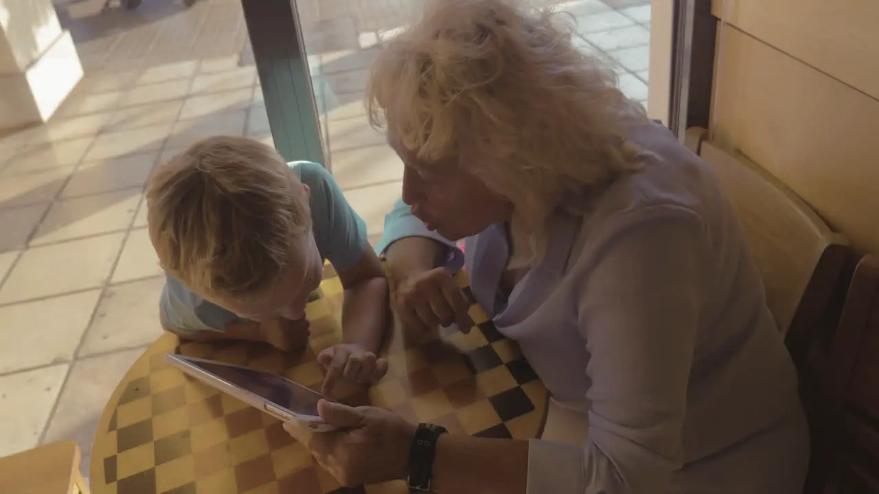 Boy and grandmother entertaining with touch pad in cafe