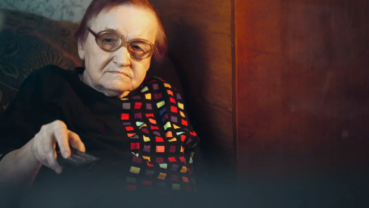 Elderly woman in glasses watching TV and changing channels