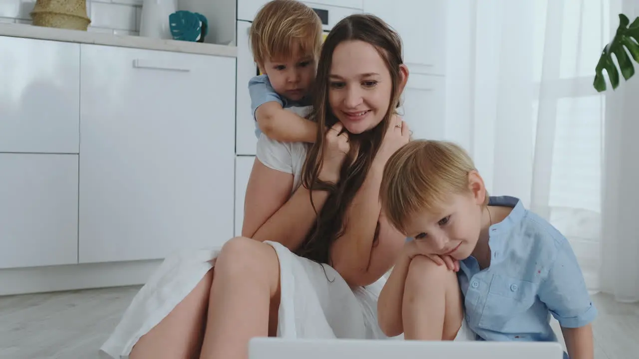 Mom and two children play sitting on the floor hugging and having fun A happy family The game after viewing the laptop Games with children