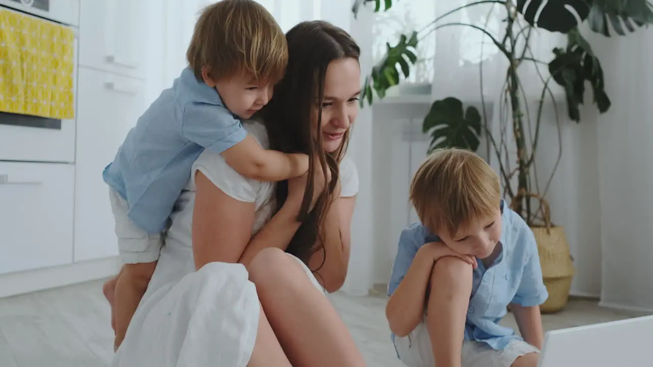 Loving mother and children hugging and having fun playing sitting on the floor Fun and happy family The game after viewing the laptop