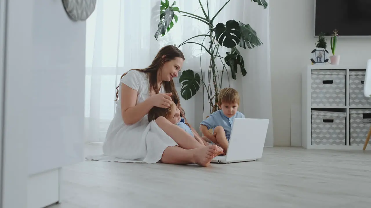 Modern apartment mom and two sons sitting on the floor in the living room look at the laptop screen