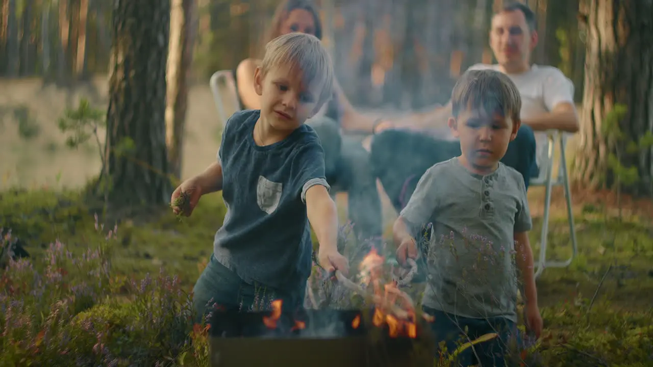 Two boys sitting by a fire against a tent in the woods on the shore of the lake fry marshmallows on fire Brothers 3-6 years together burn sticks on fire