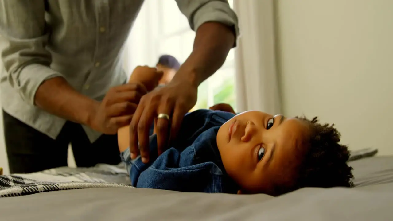 Mid section of black father helping his son changing his clothes on bed in a comfortable home 4k