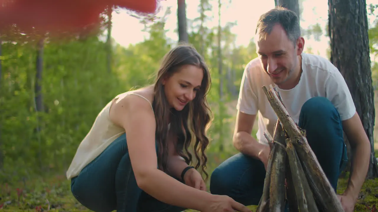 A couple man and a woman together collect a fire from sticks in the woods A young couple in a hike puts a fire for the night and cooking in nature