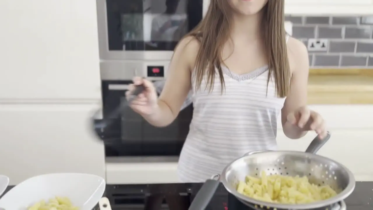 Young female making pasta and sauce in a large kitchen late at night smiling at the camera and getting embarrassed and camera shy