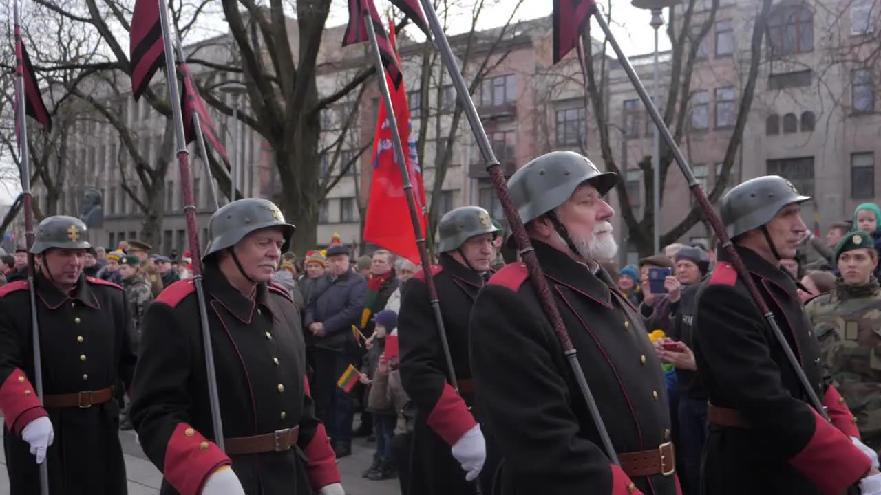 Slow motion track of disabled veterans marching down the streets of Kaunas in military dress for a celebration in Lithuania carrying flag poles