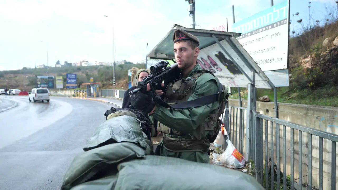 IDF soldier armed with sniper rifle behind sandbags barrier at Israeli settlement