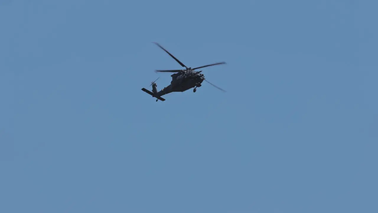 Slow motion track shot of flying black military helicopter against blue sky and sunlight