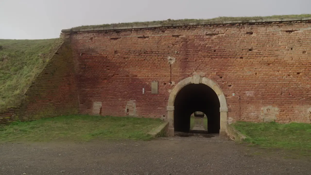 Close-up of the old brick wall of the Terezín Fortress with a small arched entrance surrounded by grass and a clear sky above