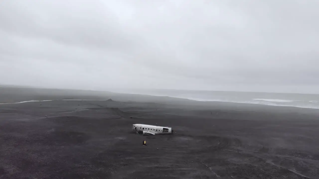 Zoom out aerial of a white plane wreck on a black beach in Iceland