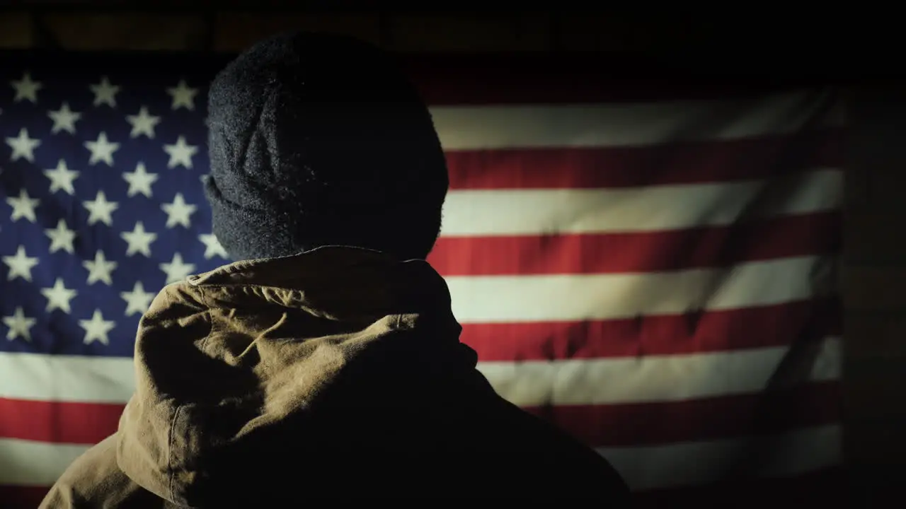 The Silhouette Of A Man -- He Looks At The American Flag On The Brick Wall The View From Behind