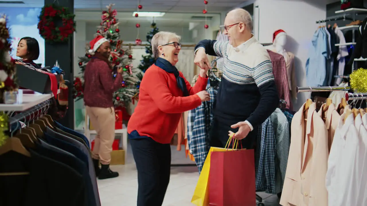 Senior man holding shopping bags spinning wife in festive decorated fashion shop happy after finding ideal presents to share with family members at Christmas event party