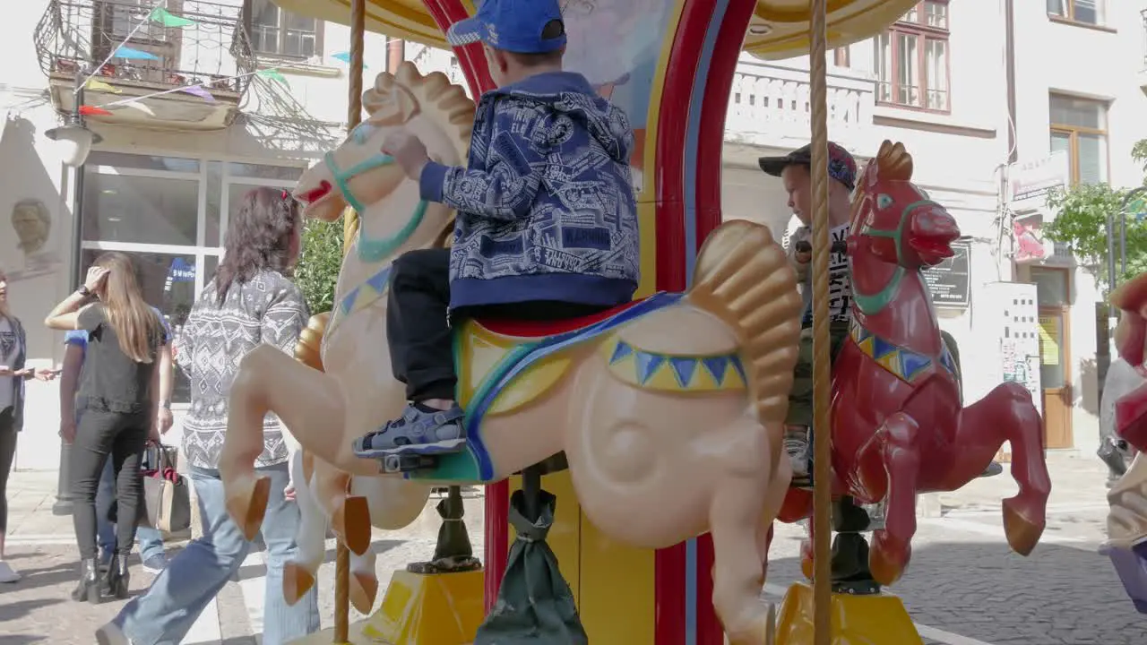 Children ride on a small children's carousel with horses