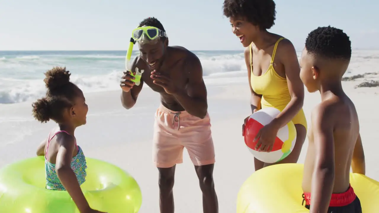 Smiling african american family with inflatables talking on sunny beach