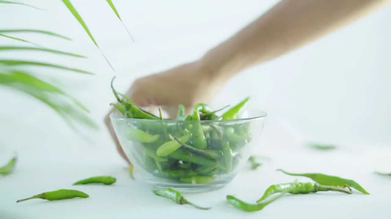 Close up shot of green chilli been collected in a glass bowl by female hands on white background