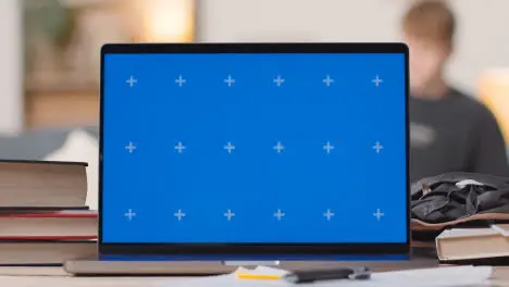 Blue Screen Laptop on Desk At Home With Student Working In Background