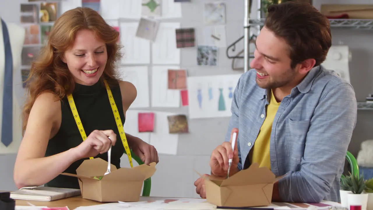 Male And Female Fashion Designers Having Working Takeaway Lunch In Studio Together