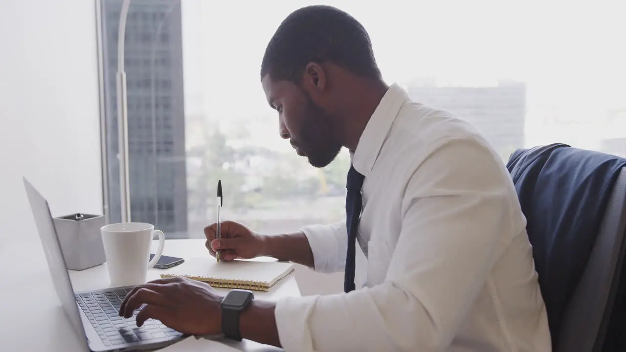 Businessman Working At Desk On Laptop In Modern Office Checking Data On Smart Watch