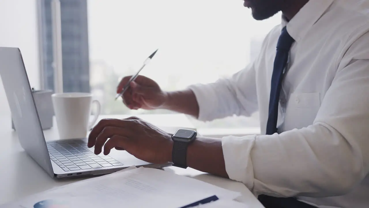 Close Up Of Businessman Working At Desk On Laptop In Modern Office Checking Data On Smart Watch